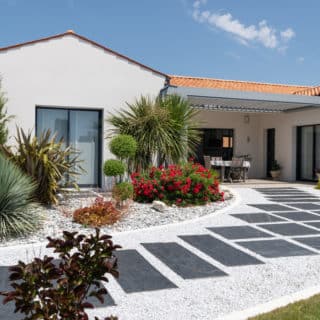Extérieur d'une maison neuve de 139 m² à Saint-Sulpice-de-Royan, avec un enduit blanc et des menuiseries gris anthracite.